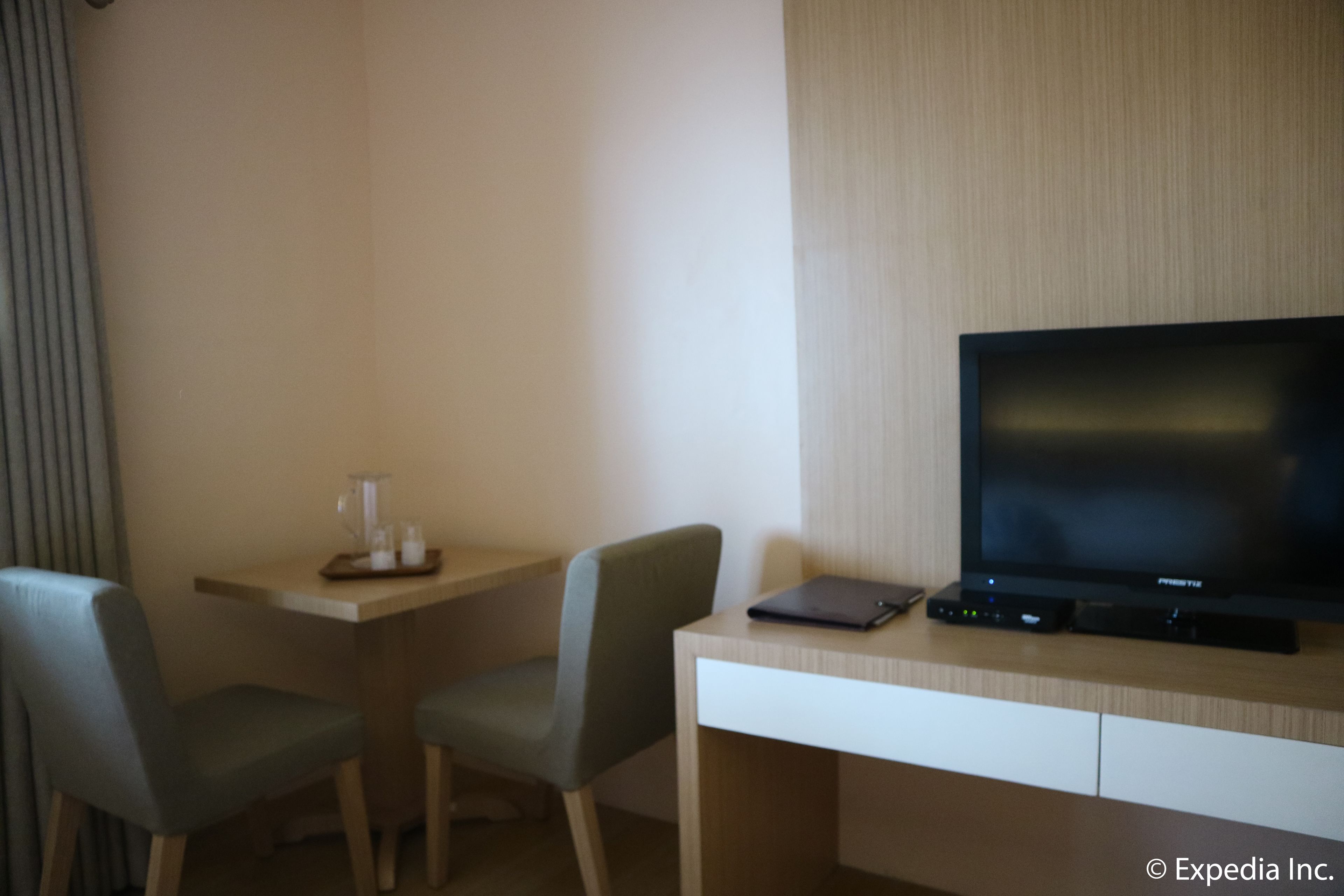 A hotel room with a wooden desk, two chairs, a television, and a small table with a glass and a tray.