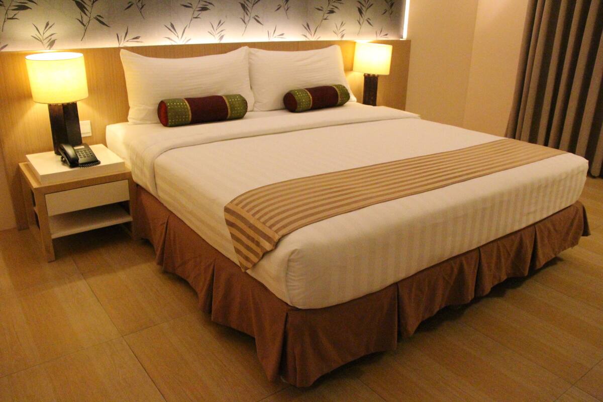 A hotel room with a large bed, two bedside lamps, a nightstand with a phone, and a wall with a leaf pattern.