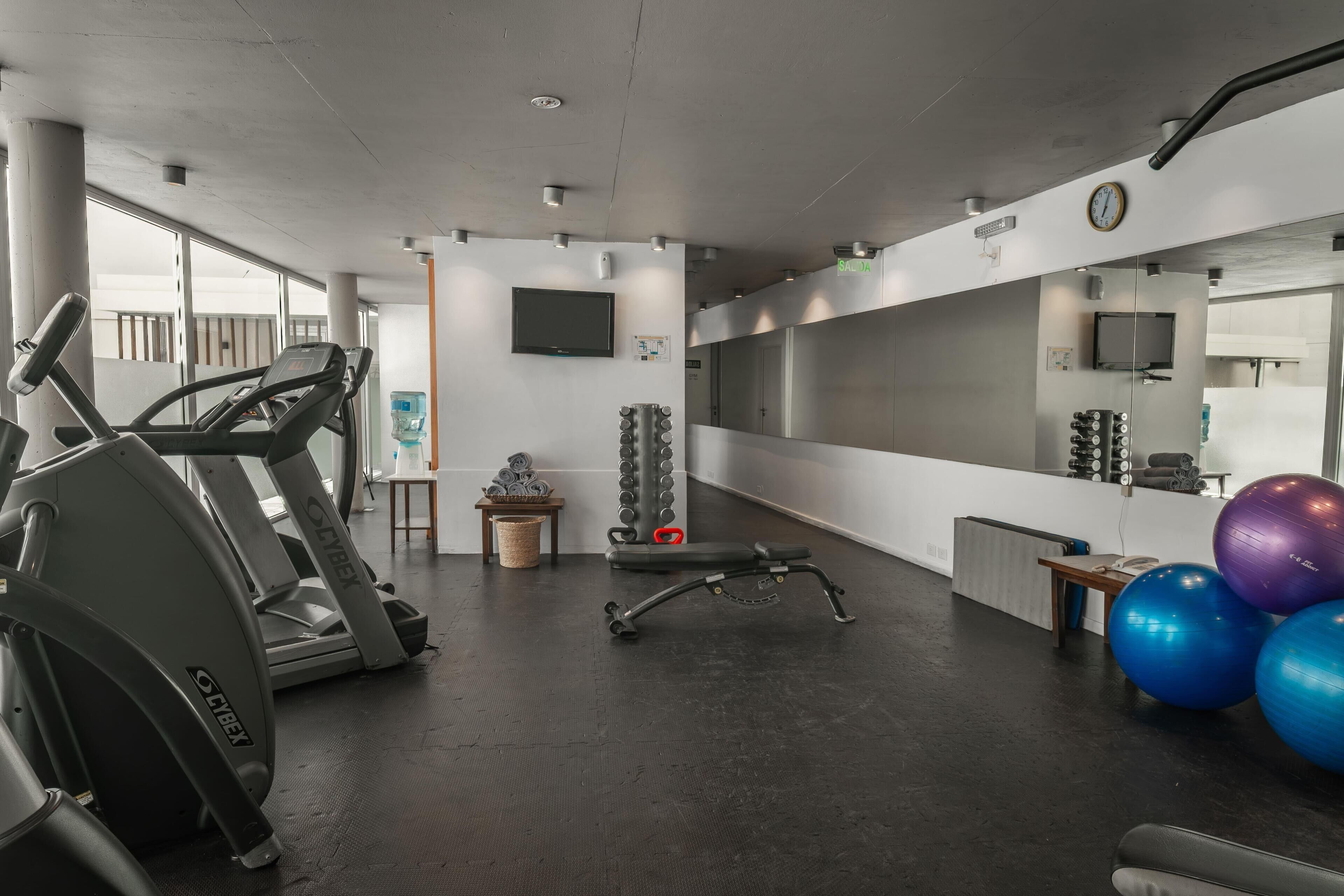 A gym with treadmills, a bench, exercise balls, and a TV on the wall.