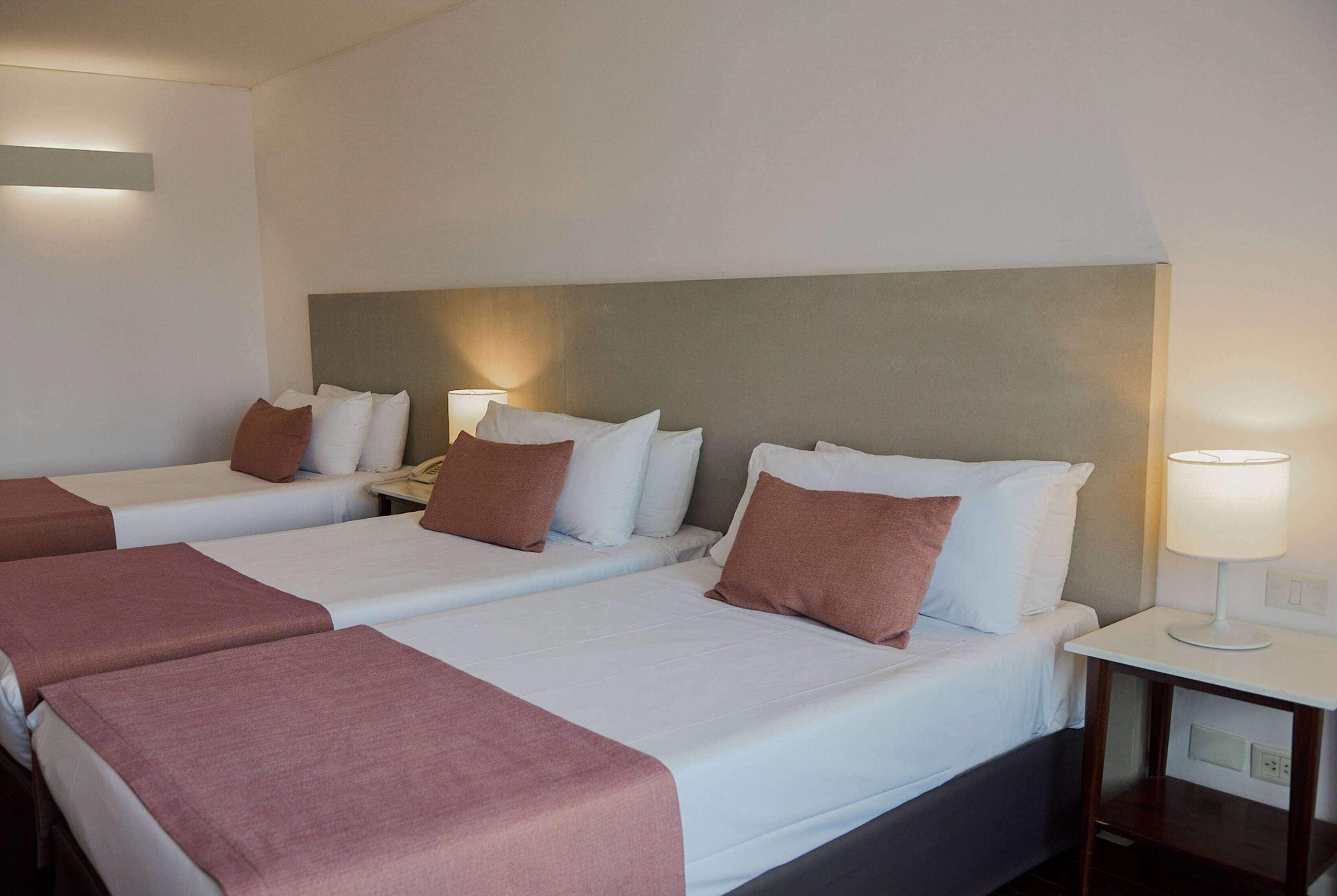 A hotel room with two beds, each with white linens and brown pillows, and a bedside table with a lamp.