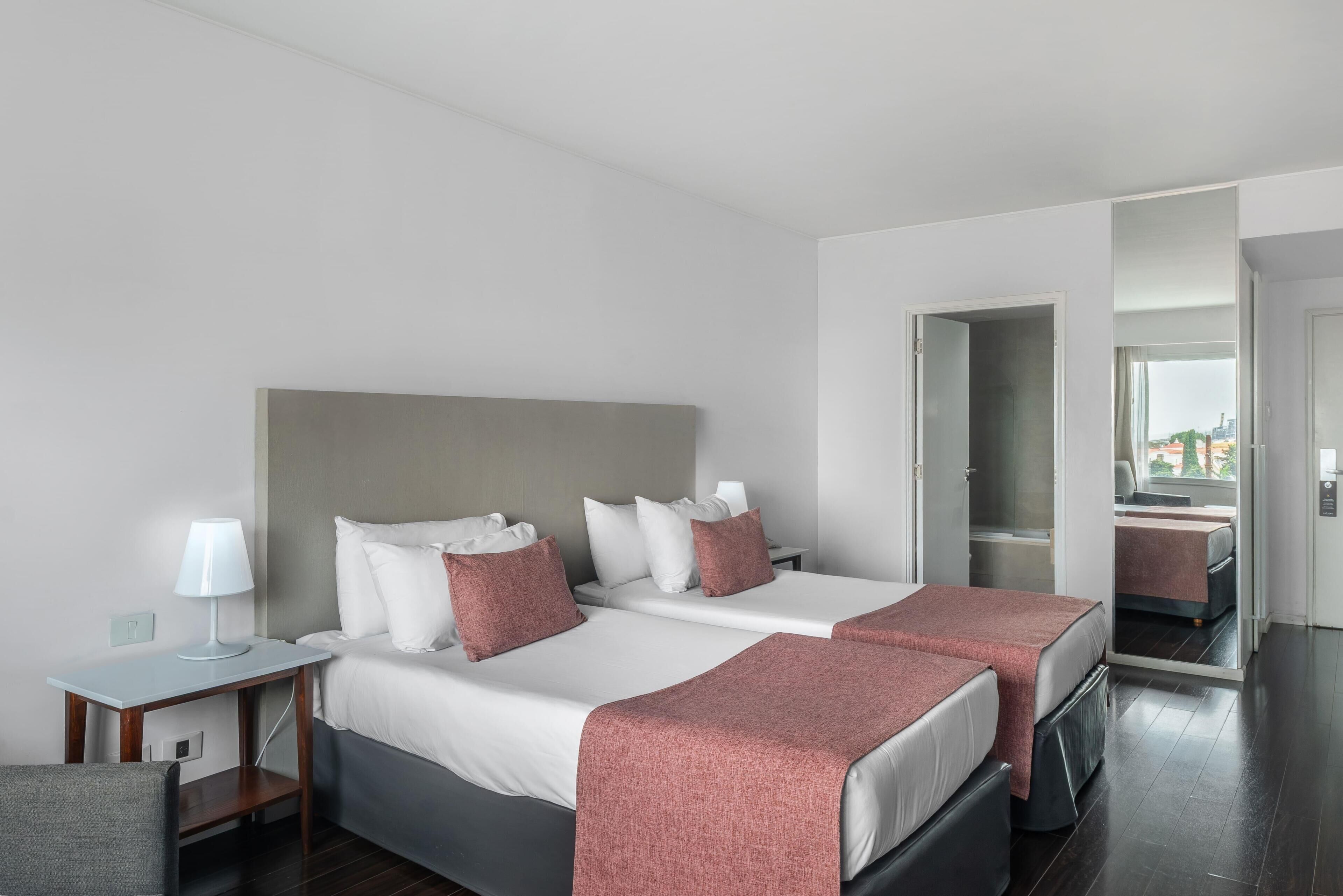 Habitación de hotel con dos camas, un escritorio con lámpara y un espejo.