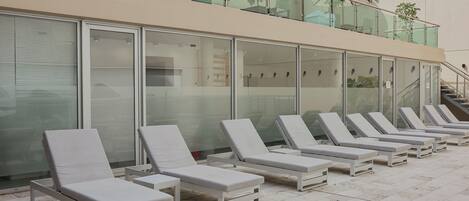 A row of white lounge chairs with metal frames, arranged on a tiled patio area.