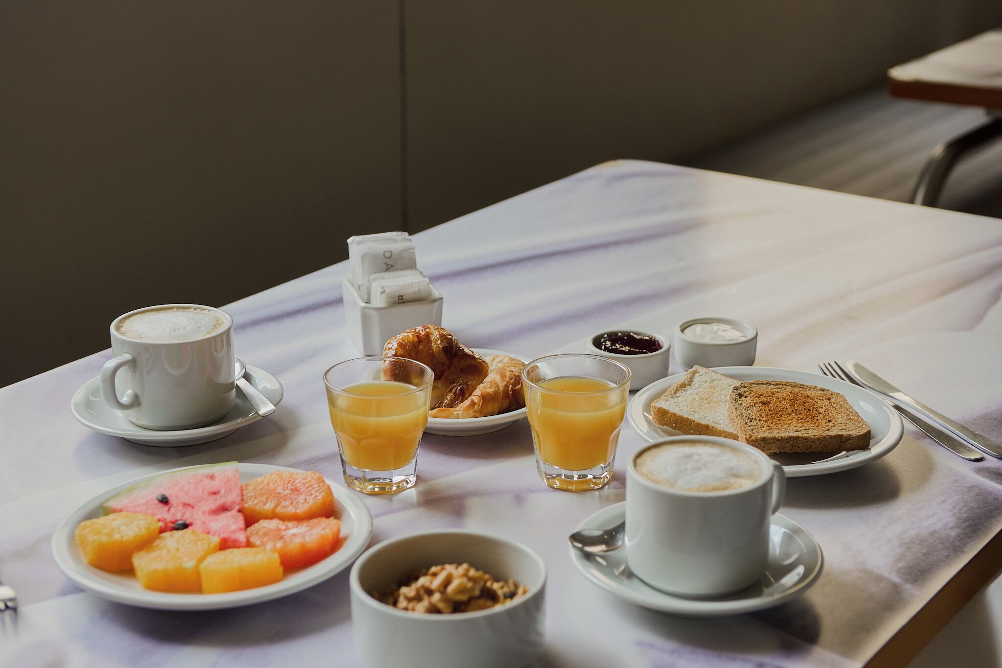 A breakfast table with croissants, orange juice, coffee, toast, and fruit.