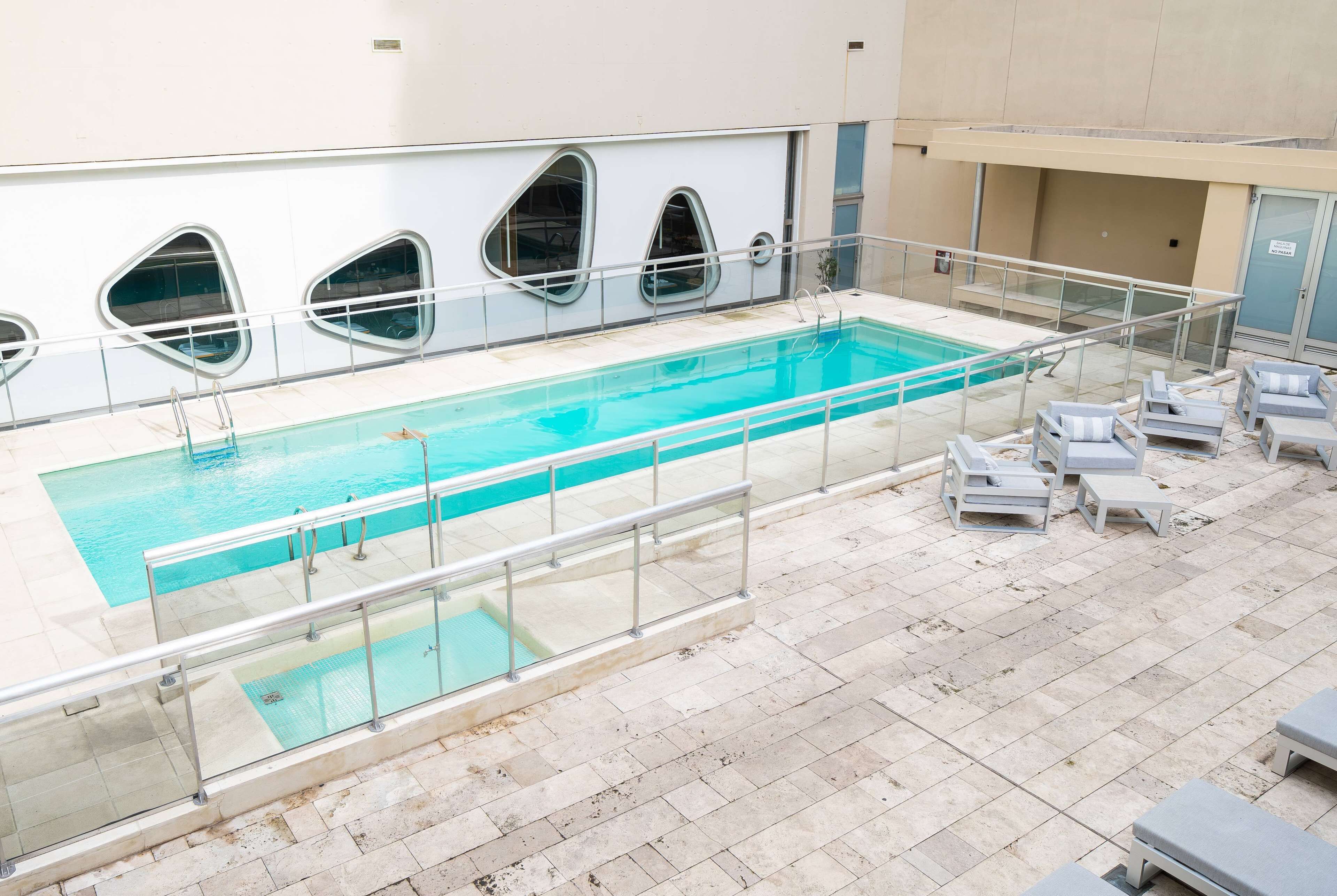 An indoor swimming pool with clear water, surrounded by a tiled deck and lounge chairs.