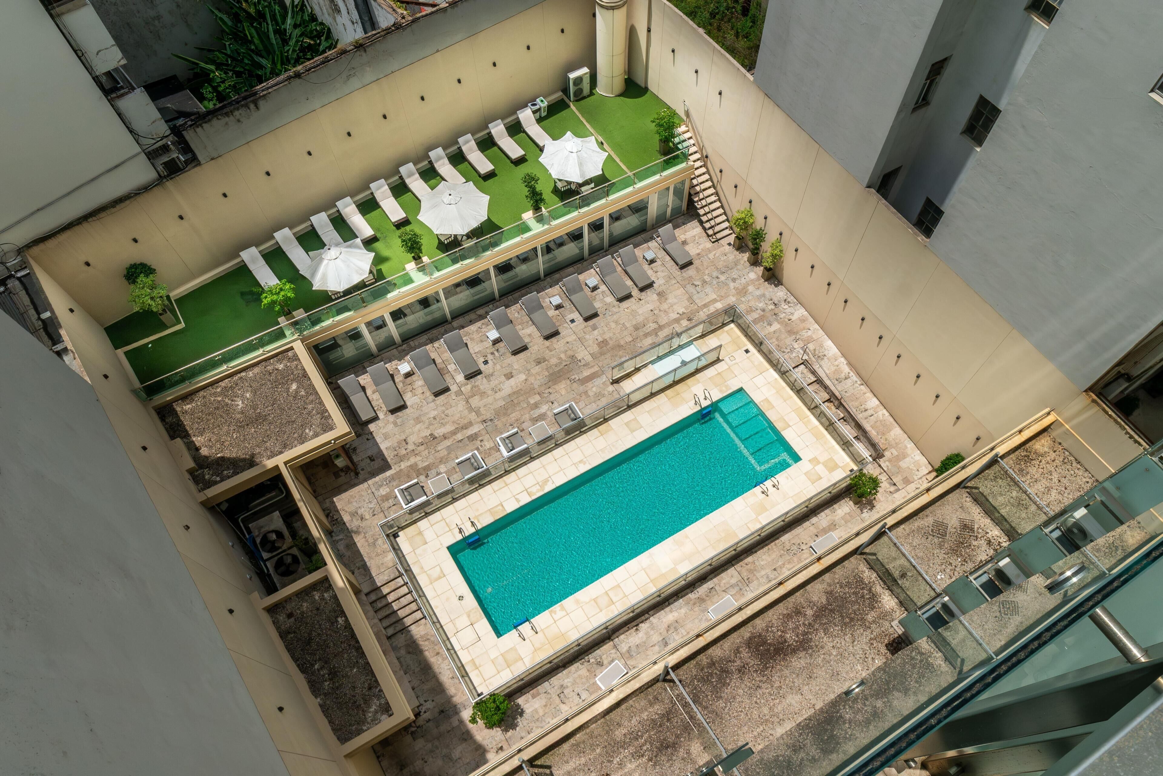 An aerial view of a rooftop pool area with lounge chairs, umbrellas, and a swimming pool.