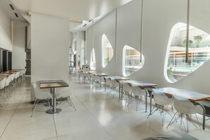 Un espace de restauration moderne avec des tables et des chaises blanches, de grandes fenêtres et un design épuré et minimaliste.