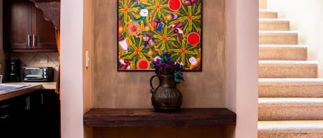 A dining area with a table set for two, a vase with flowers, and a colorful artwork on the wall.