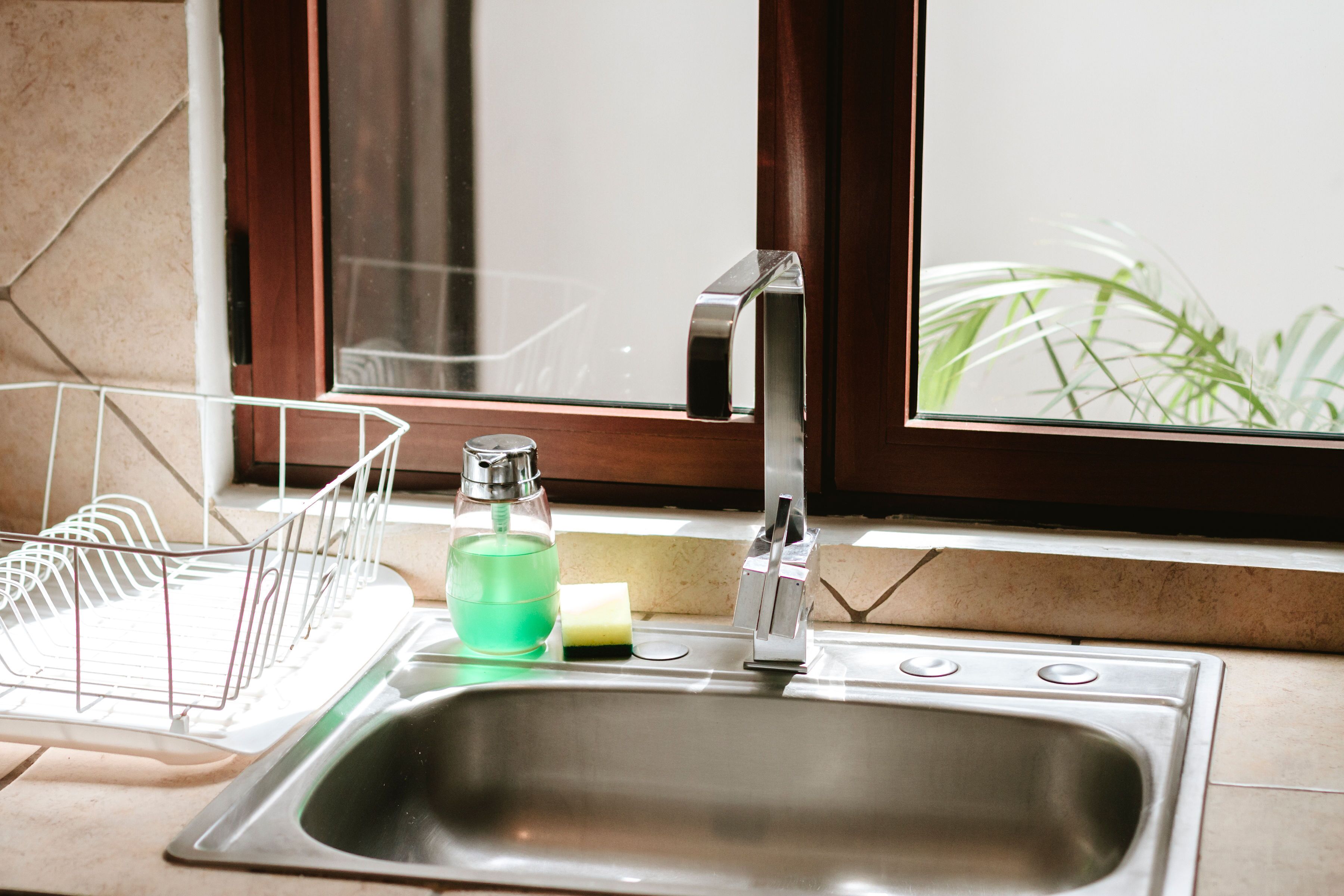 Una lavandino da cucina con un espositore per piatti, un dispenser di sapone e una finestra vista verde.