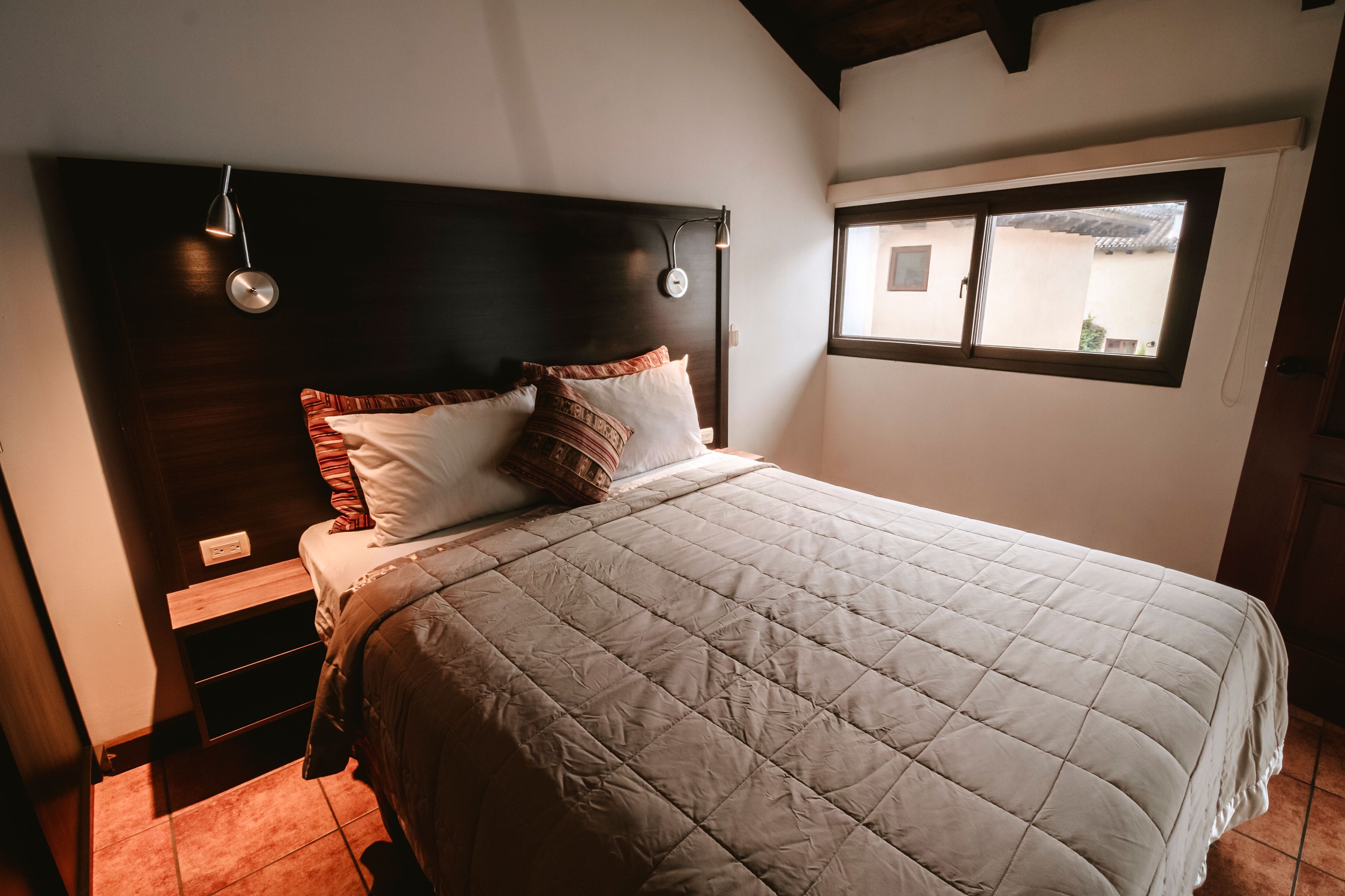 Una cama bien tendida con un edredón blanco acolchado, un cabecero de madera oscura y dos lámparas de noche.