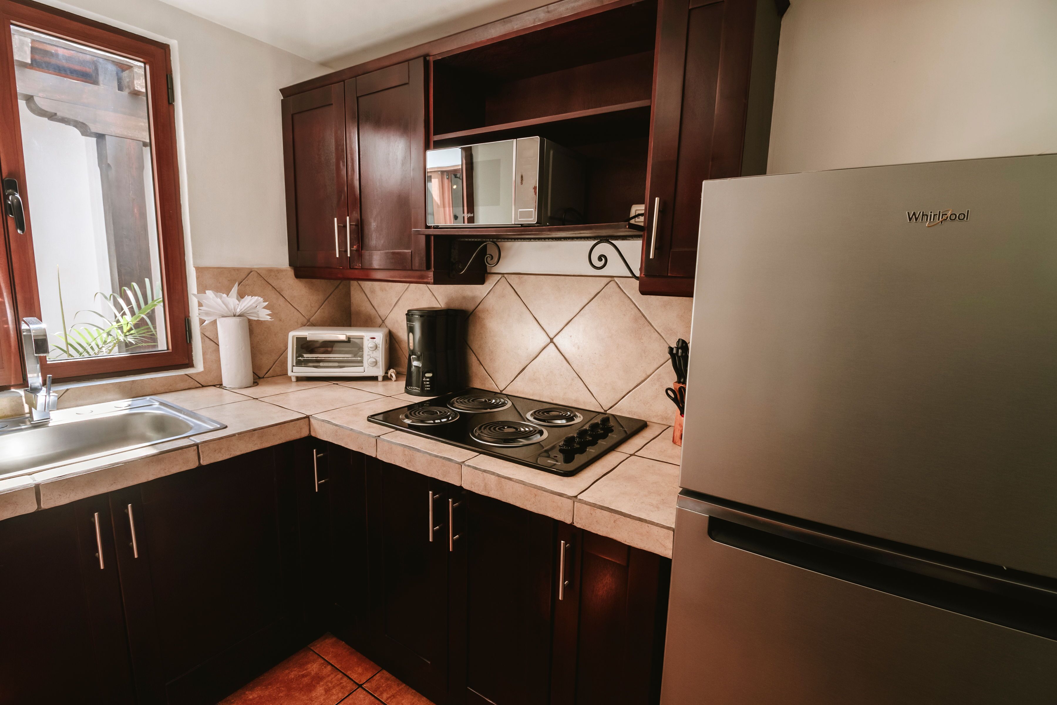 Una cocina con armarios de madera oscura, un refrigerador de acero inoxidable, un microondas, una estufa y una ventana con una planta.