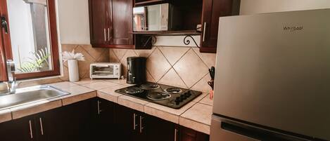 A kitchen with dark wooden cabinets, a stainless steel refrigerator, a microwave, a stove, and a window with a plant.