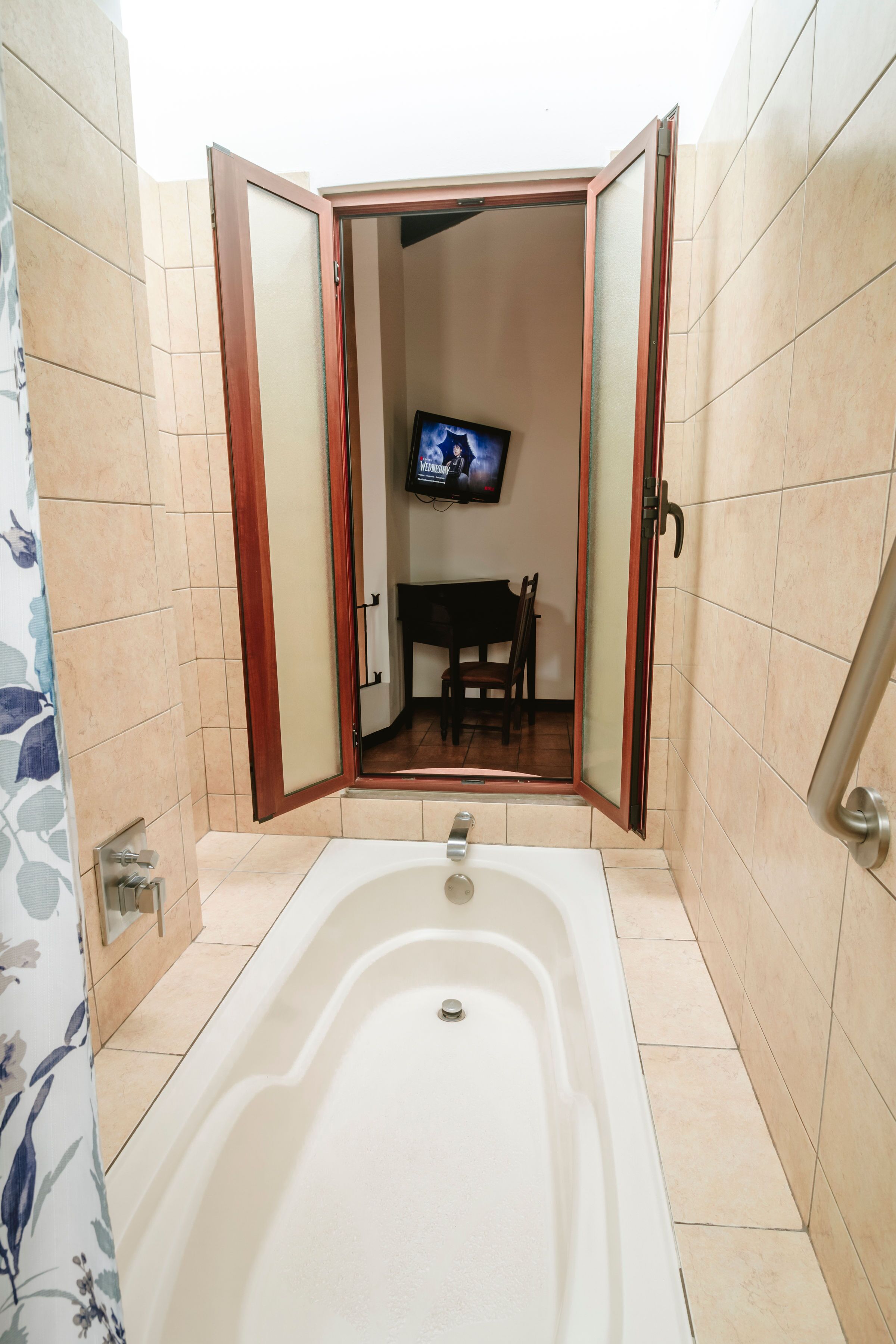 A bathroom with a bathtub, a television mounted on the wall, and a chair in the corner.