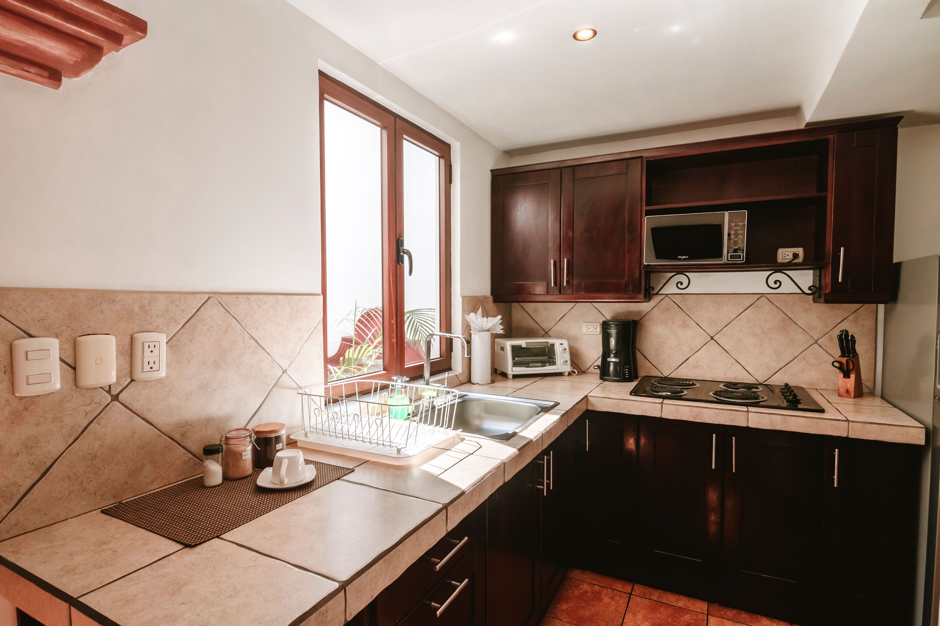 Una cocina con microondas, tostadora y estufa. Hay armarios, un lavaplatos y una ventana con vistas.