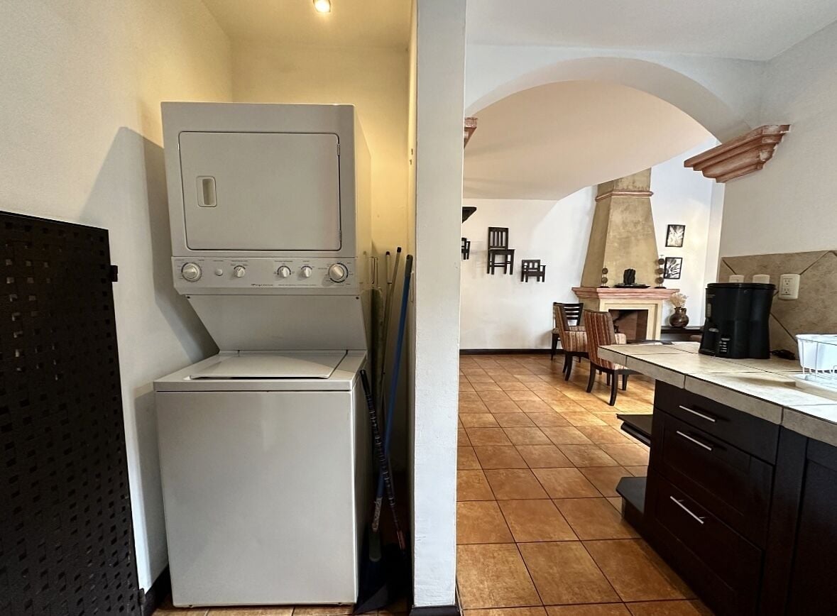 A compact kitchen with a washing machine, a dining area with chairs, and a tiled floor.