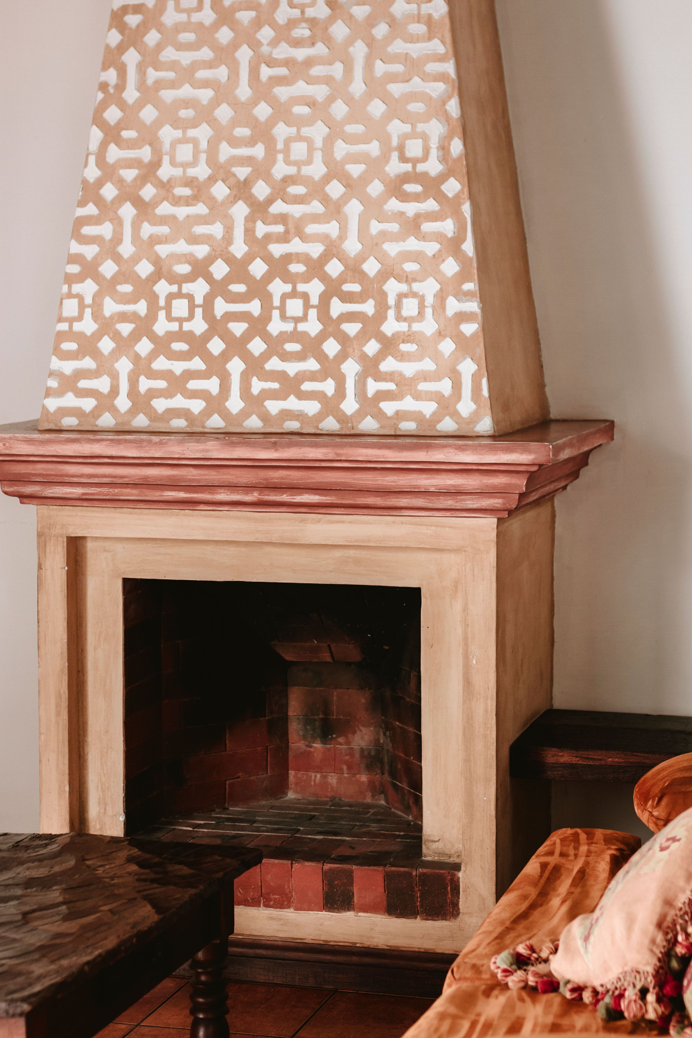 Una chimenea con un protector geométrico, un fuste de madera y un interior de ladrillo.