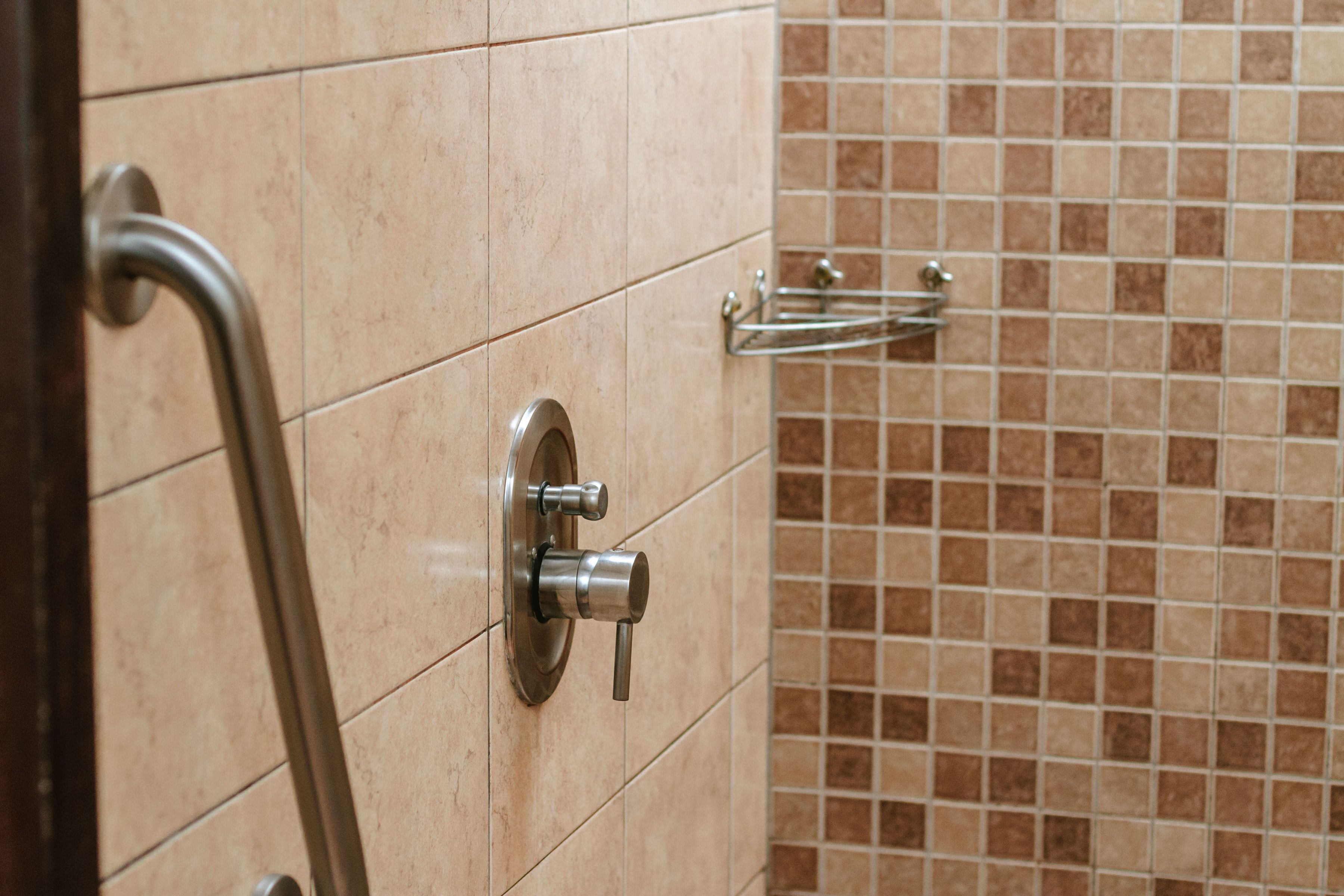 A bathroom with beige tiles, a handrail, and a towel rack.