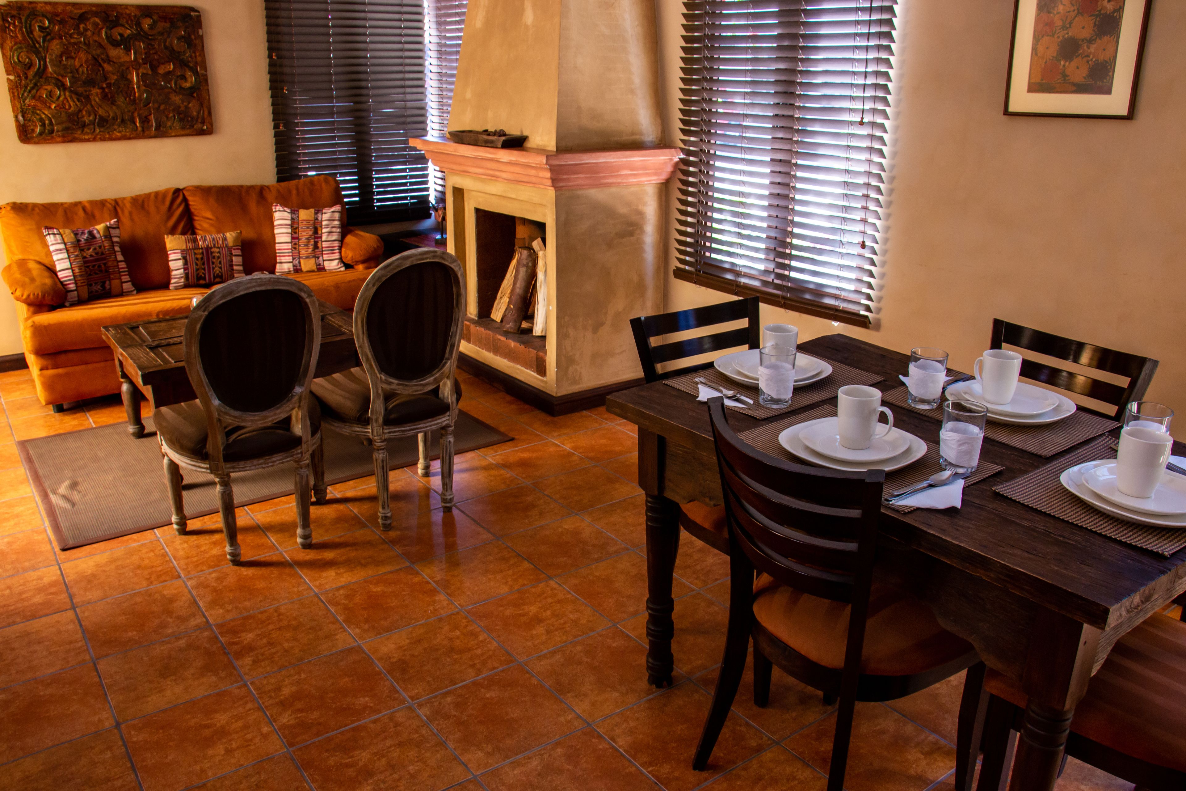 Un coin repas avec une table en bois dressée pour quatre personnes, entourée de chaises, et une cheminée en arrière-plan.