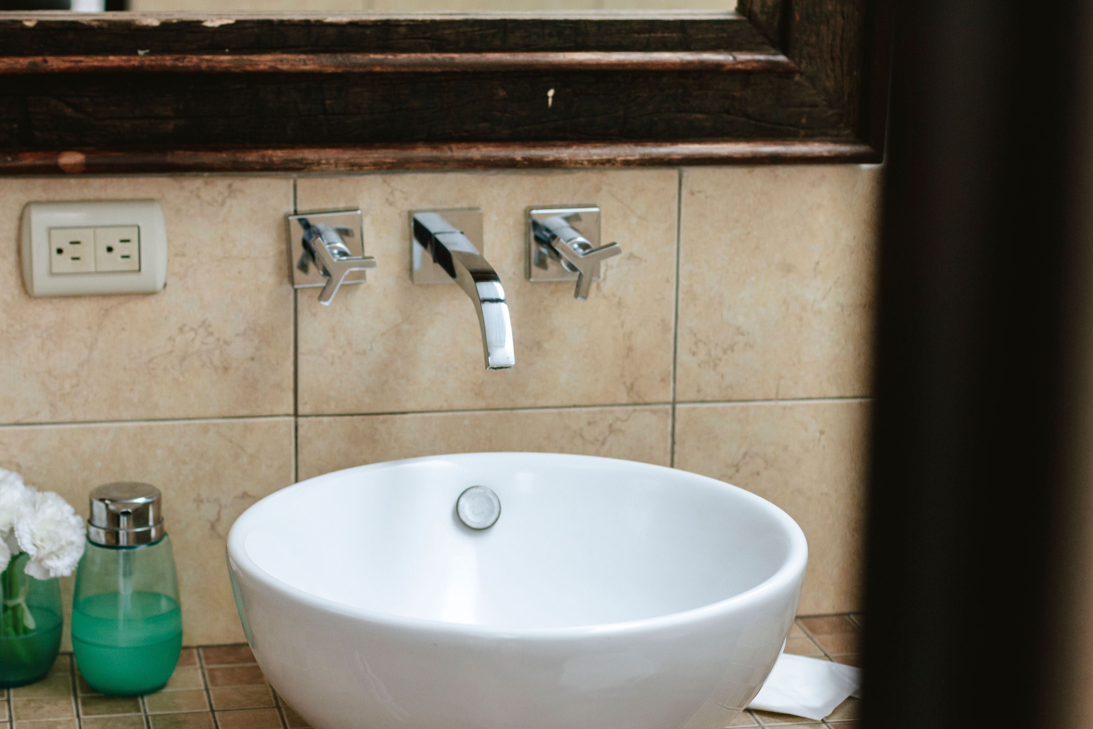 Un baño con un lavabo blanco, dos grifos y un espejo sobre el lavabo.