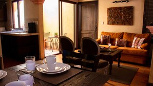 A dining area with a wooden table set for two, a sofa with patterned cushions, and a decorative wall piece.