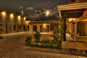 A courtyard with cobblestone flooring, a building with a tiled roof, and a mountain in the background. - All Suite El Marques de Antigua (Antigua Guatemala)