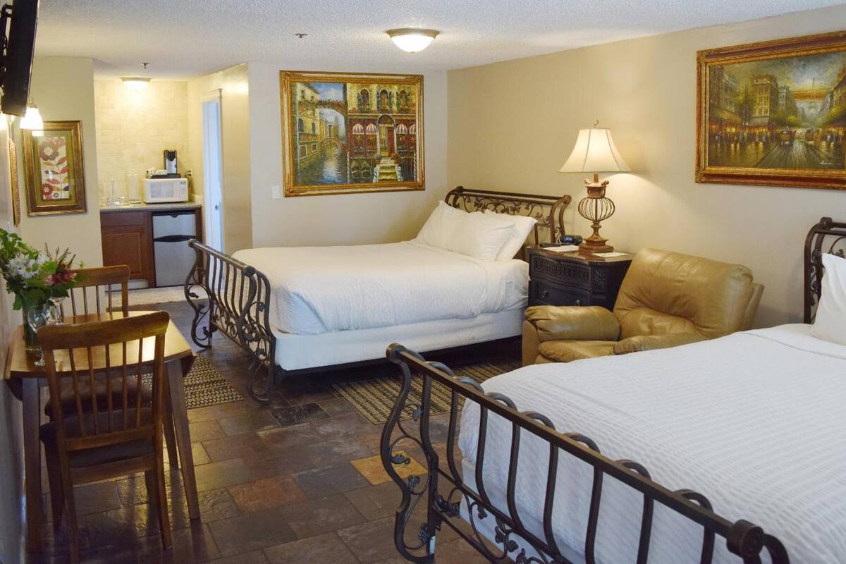Habitación de hotel con dos camas, un escritorio, una silla, una lámpara y cuadros en las paredes.