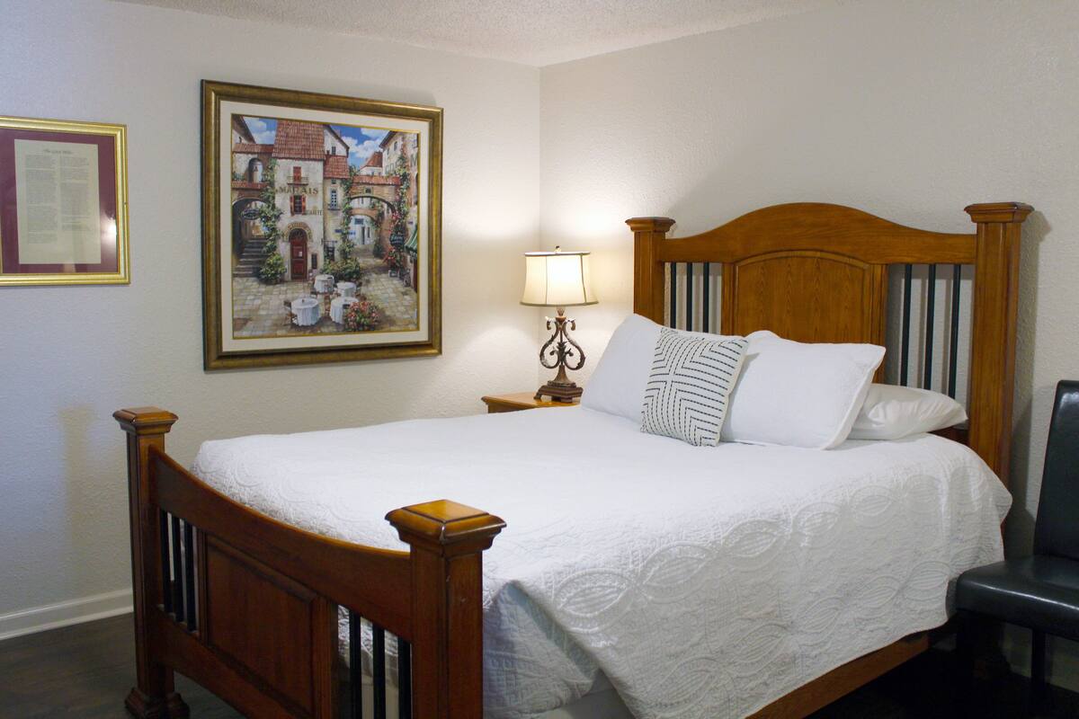 Una cama bien hecha con cabecera de madera, una lámpara de noche y un cuadro enmarcado en la pared.