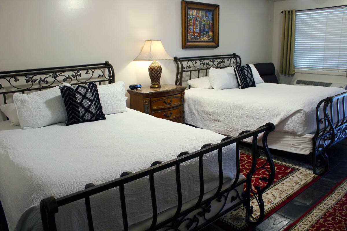 Una habitación de hotel con dos camas, una mesita de noche con lámpara, una silla y un cuadro en la pared.