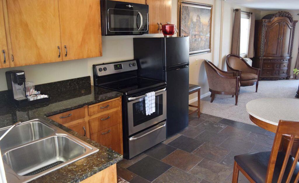 A kitchen with a stainless steel sink, a black stove, a microwave, and a refrigerator.