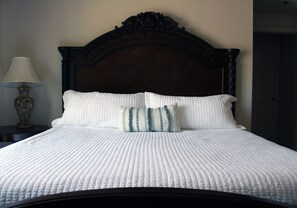 A neatly made bed with a white quilt and two pillows, a dark wooden headboard, and a bedside table with a lamp.
