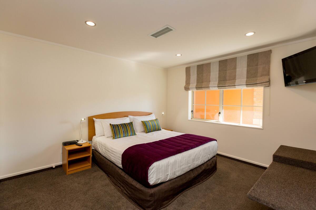 A neatly arranged bedroom with a bed, bedside table, and a window with blinds.
