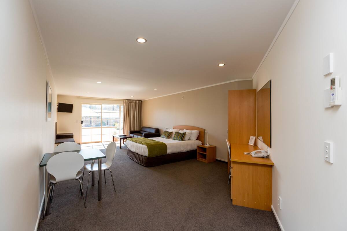 A hotel room with a bed, bedside table, chair, desk, and a window.