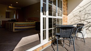 A bedroom with a bed, a window, and a sliding glass door leading to an outdoor patio area with a table and chairs. - Aspen Court Motel Taihape (Taihape)