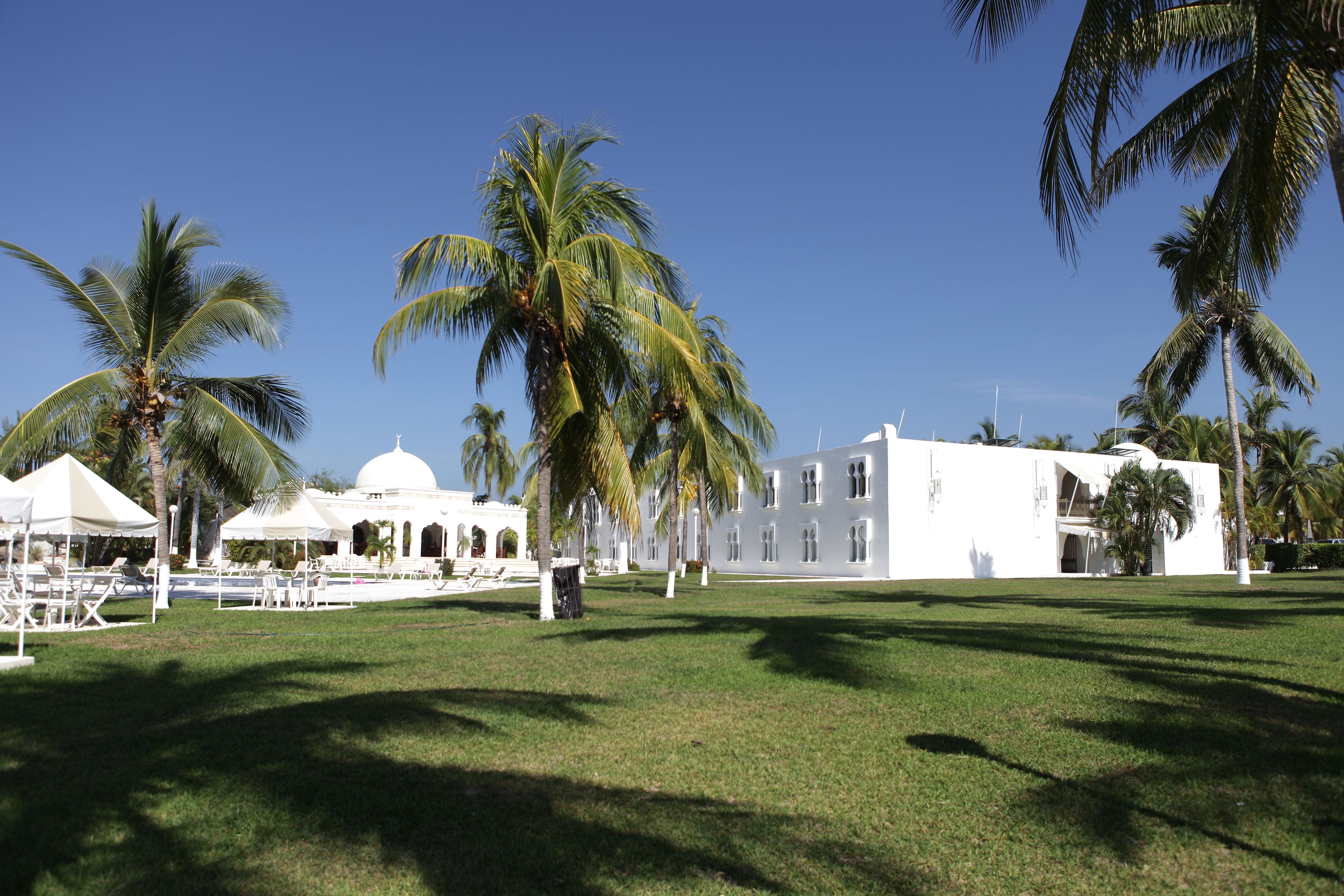 Un edificio blanco con cúpula, rodeado de palmeras y un césped cuidado.