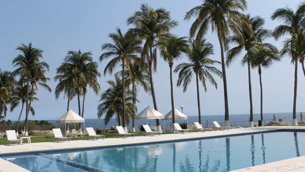 Piscina con sillas de descanso y palmeras, con vista al océano.
