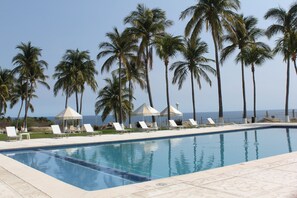A swimming pool with lounge chairs and palm trees, overlooking the ocean. - Hotel Aldea del Bazar (Puerto Escondido)
