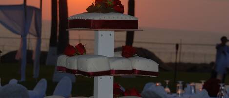 Un pastel de bodas de varios niveles con rosas sobre una mesa al aire libre, con un atardecer de fondo.