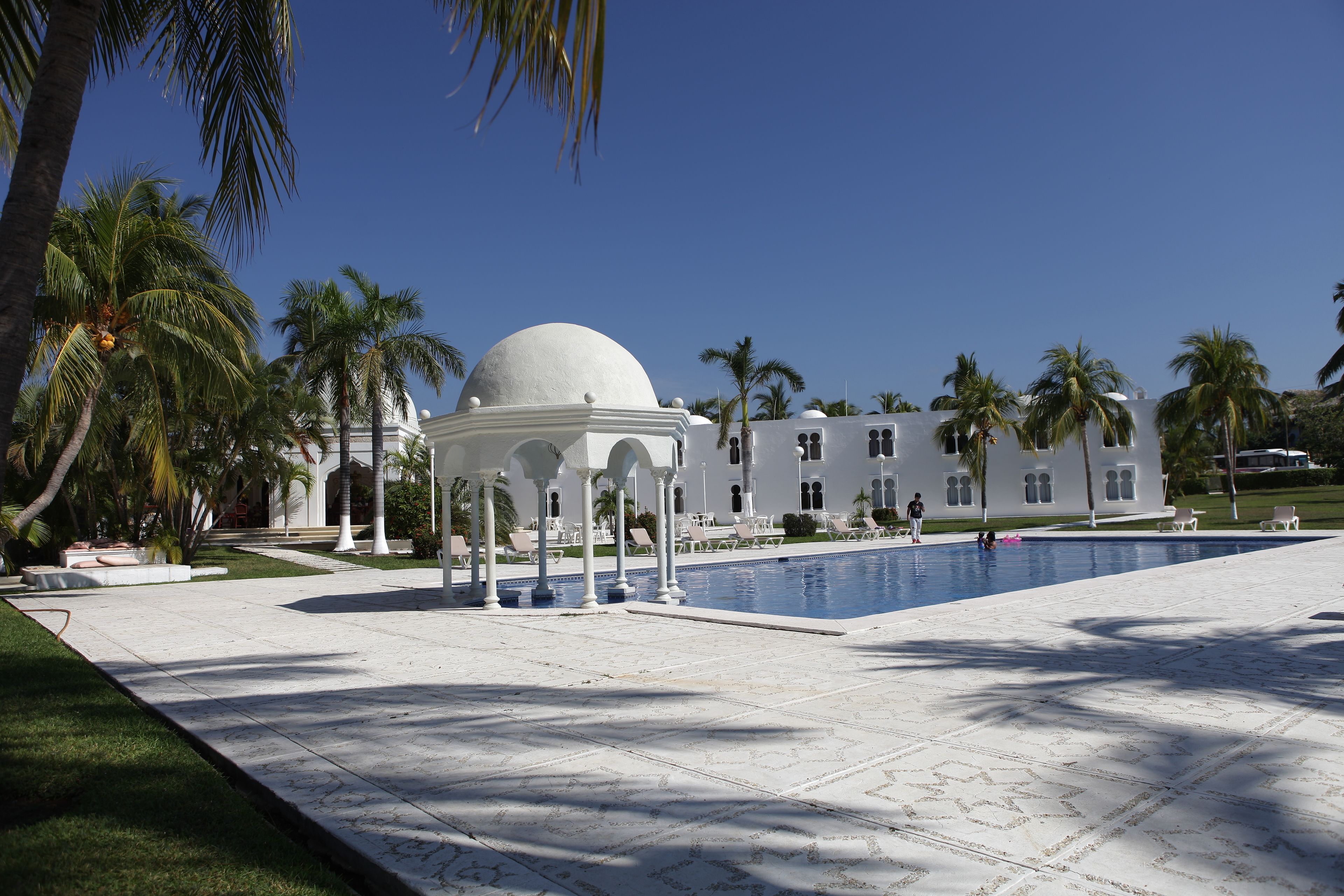 Un edificio blanco con una cúpula y columnas, piscina y palmeras.