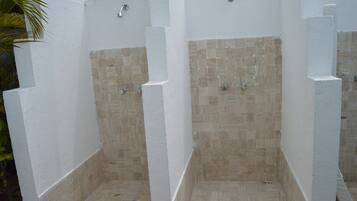 Tres cabinas de ducha con revestimiento de azulejos blancos y mosaicos beige en las paredes.