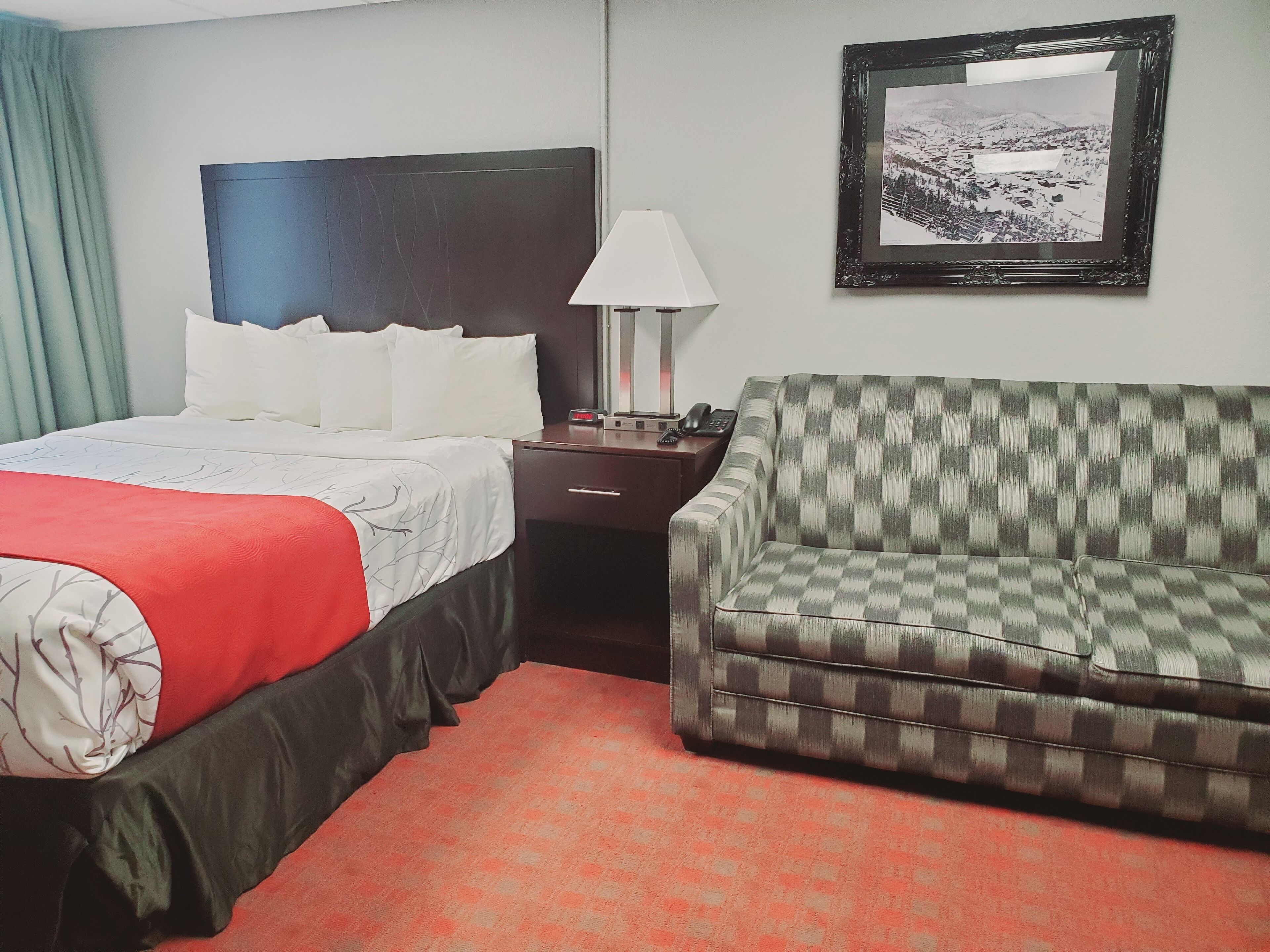 Een hotelkamer met een bed, een bank, een nachtkastje, een lamp en een lijst met een foto aan de muur.