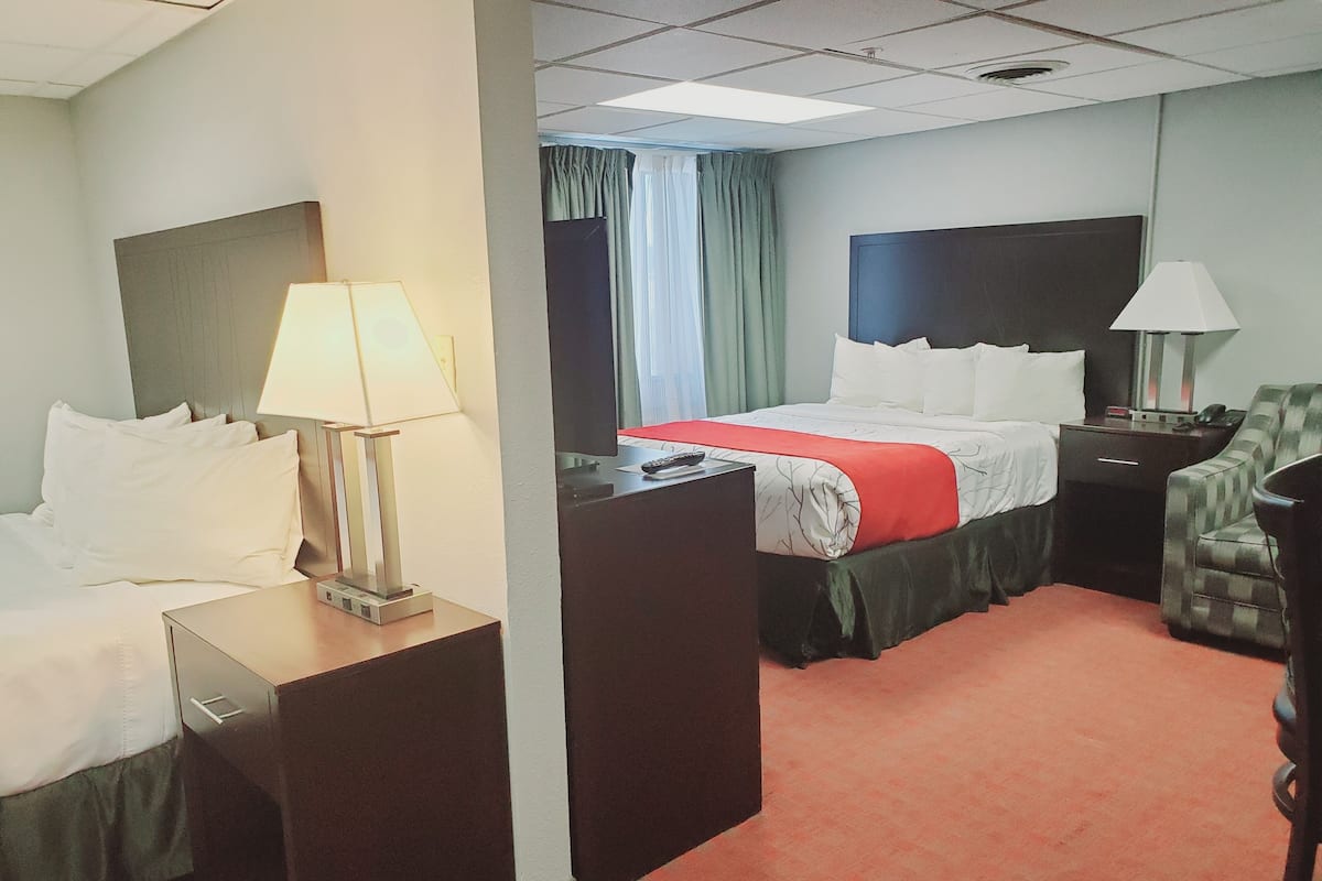 A hotel room with a bed, two bedside tables, a desk, a chair, a TV, and a window with curtains.