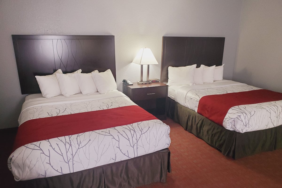 A hotel room with two beds, each with a red and white bedspread, a nightstand with a lamp, and a telephone.