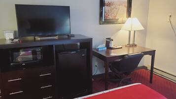 Una habitación de hotel con una cama, un escritorio con lámpara, un televisor, un microondas y una cafetera.