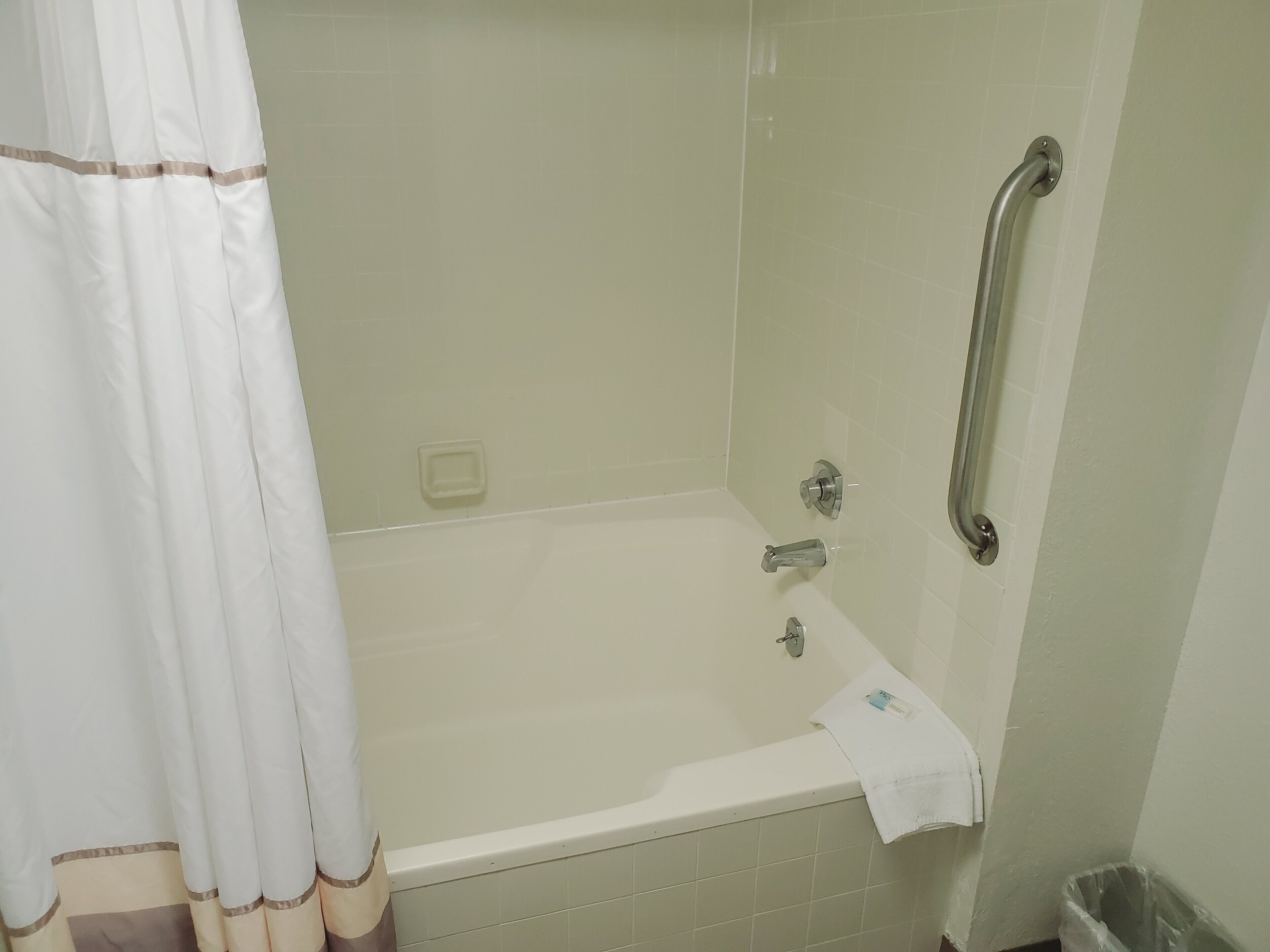 A bathroom with a bathtub, a shower with a grab bar, and a trash bin.