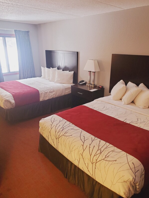 A hotel room with two beds, a nightstand with a lamp, and a window with curtains.
