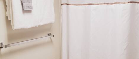 A bathroom with a shower curtain, a towel rack with a folded towel, and a wall-mounted towel.