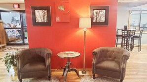 Een kamer met twee fauteuils, een tafeltje, een lamp en lijstjes met foto's aan de muur.