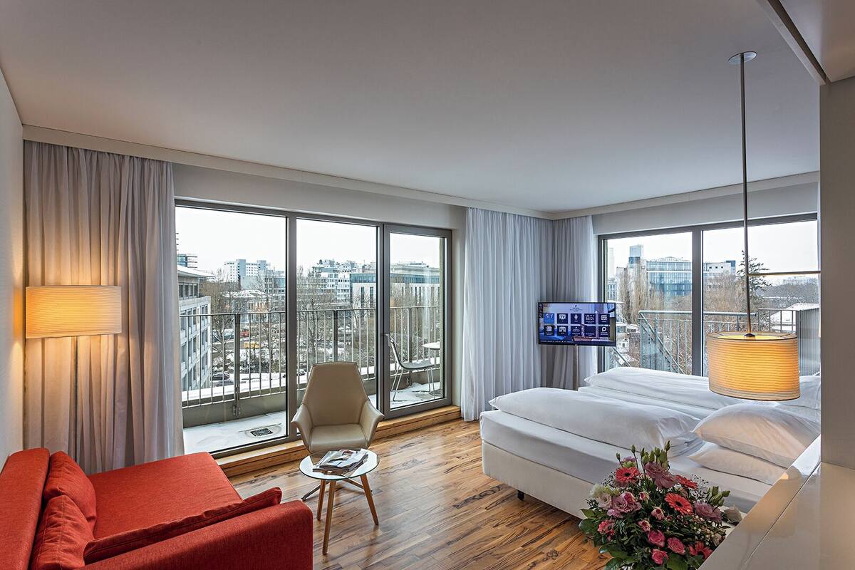 A modern hotel room with a large bed, a red sofa, a small table, and a TV.