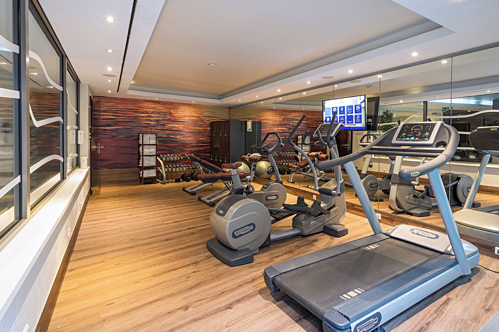 Een moderne sportschool met diverse fitnessapparaten, waaronder loopbanden en gewichtmachines, en een scherm dat trainingsopties toont.