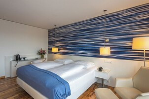 Una camera d'albergo moderna con un letto grande, lampade sui comodini, un tavolino con il telefono e una sedia.