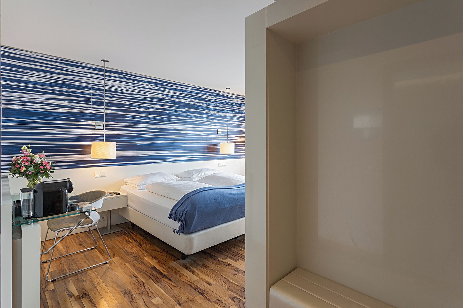 Una habitación de hotel moderna con cama, mesita de noche y un detalle decorativo en la pared.